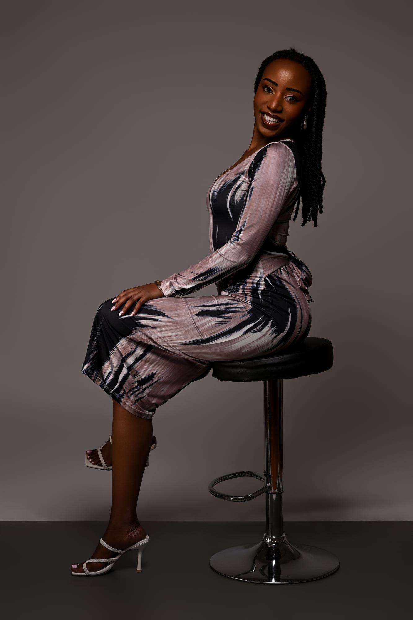 Lorna Ishimwe seated on a studio stool, printed midi dress, relaxed editorial posture.