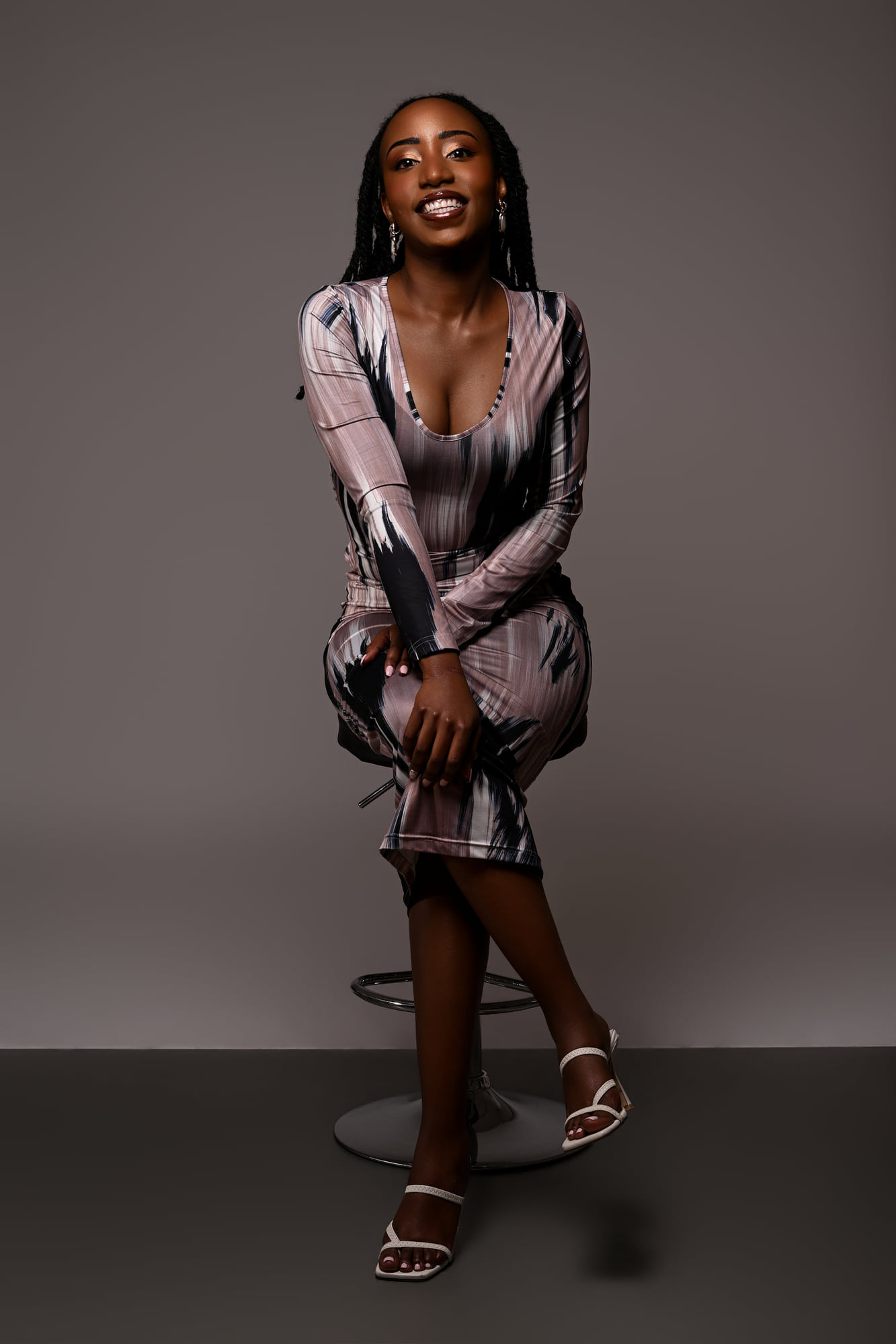 Lorna Ishimwe standing in a printed midi dress and heeled sandals, full-length studio frame.