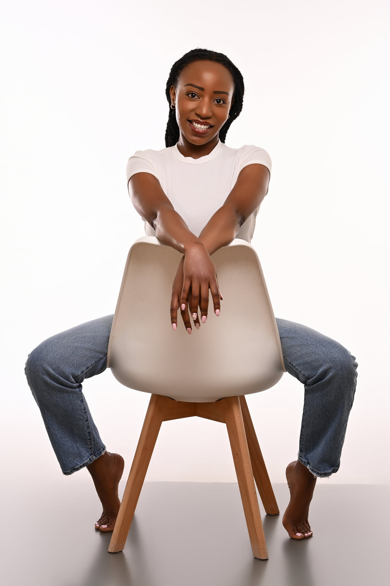 Lorna Ishimwe leaning on a studio chair in a white t-shirt and denim.