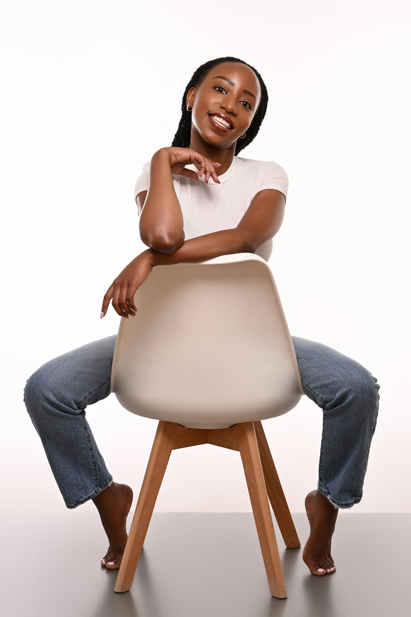Lorna Ishimwe seated with chin resting on hand, white t-shirt and denim in studio.